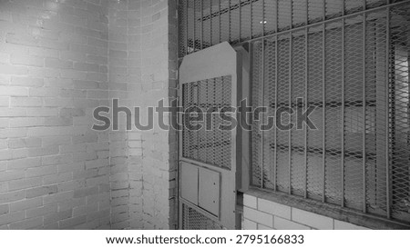 Abandoned Prison Cell Block Interior with Steel Security Bars, Expanded Mesh Panel and White Brick Wall — Black and White Institutional Photography
