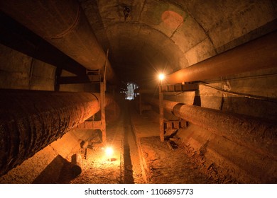 Abandoned round concrete underground tunnel of heating main with rusty tubes.