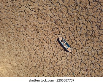 Abandoned row boat on cracked soil on lake bed dried up due to global warming and drought
