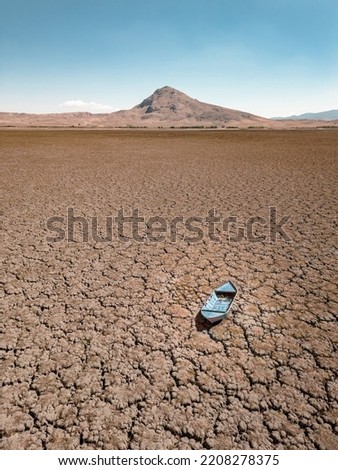 Abandoned row boat on cracked soil on lake bed dried up due to global warming and drought