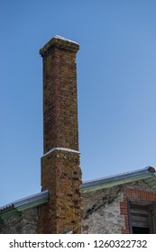 Abandoned Ruin Of Oven Chimney. Broken Furnace. Snowy Roof And Blue Sky Background In The Winter