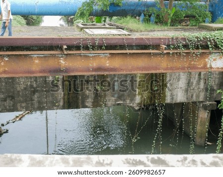 Abandoned and rusting bridge over a small river, overgrown with creeping plants in an urban environment. Symbol of urban decay and nature reclaiming manmade structures.
