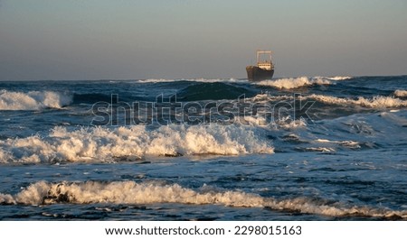 Abandoned ship in the stormy sea with big wind waves at sunset. Shipwreck in the ocean.