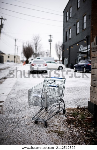 Abandoned shopping cart in\
the snow in a widely spaced alleyway with fresh snowfall covering\
the street.