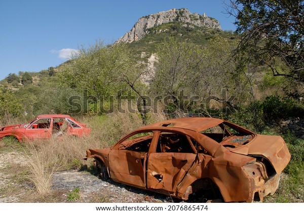 Abandoned stolen cars in the\
countryside, one of them burnt out and rusted. Environmental\
pollution.