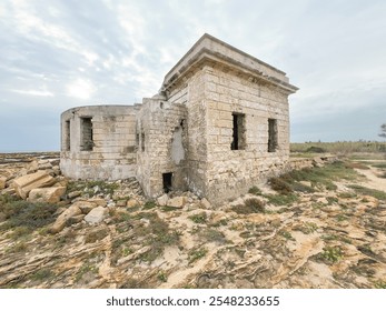 Abandoned stone building by the rocky coastline, surrounded by rugged terrain and a cloudy sky, symbolizing history and decay - Powered by Shutterstock