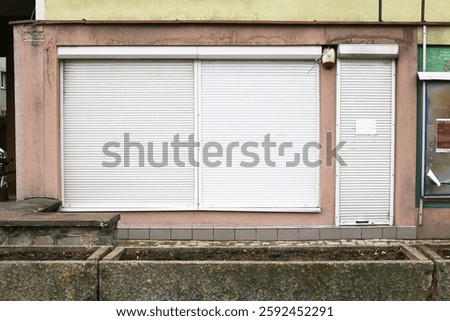 Abandoned store with closed security shutters. Grunge building facade with industrial metal roll-up doors. Urban decay and forgotten commercial space with a worn concrete exterior.