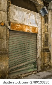 An abandoned storefront features a rusted, graffiti-tagged shutter. Left by former owners, the decaying building stands as a stark testament to urban neglect and the passage of time.