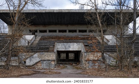 An abandoned structure surrounded by bare, tall trees. An abandoned football stadium in Pripyat. Overgrown with trees ruins of the stadium. - Powered by Shutterstock