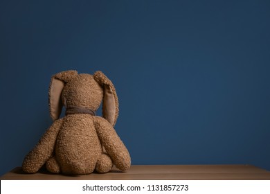 Abandoned Toy Bunny On Table Against Dark Background. Time To Visit Child Psychologist