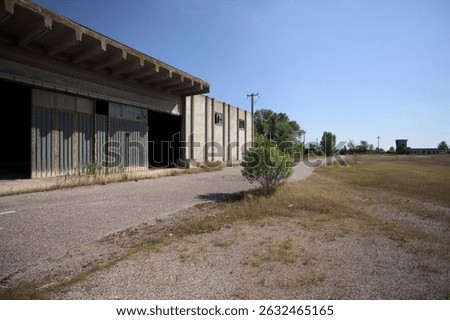 Abandoned warehouse and a paved access path to it seen from a bare yard in front of it