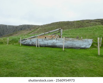 Abandoned wooden boat. Cornish coast, grass fields, hills, protective wooden posts, Spring. UK - Powered by Shutterstock