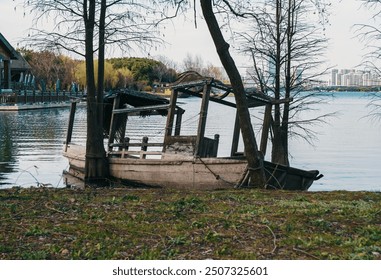 Abandoned wooden boat on shoreline of tranquil lake surrounded by trees and urban landscape - Powered by Shutterstock