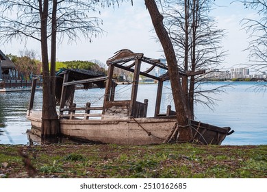 Abandoned wooden boat on shoreline of tranquil lake surrounded by trees and urban landscape - Powered by Shutterstock