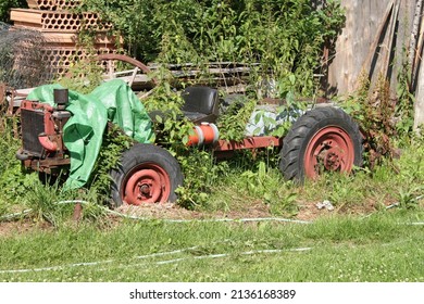 The abandoned wreck of a homemade tractor standing in the garden, overgrown with plants. 