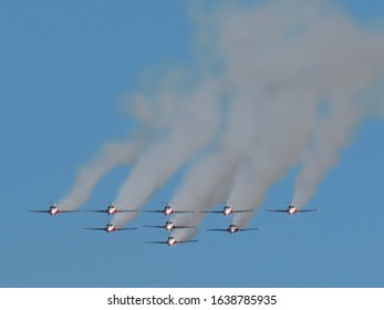 Abbotsford, BC / Canada - August 7 2015: Canadian Snowbird Demonstration Jet Flying Team in formation with headlights shining and fuel smoke streams visible behind them, silhouetted against blue sky