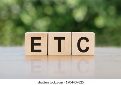 ETC (abbreviation of et cetera) word written on wooden blocks. The text is written in black letters and is reflected in the mirror surface of the table.