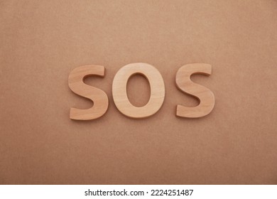 Abbreviation SOS Made Of Wooden Letters On Light Brown Background, Top View