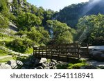 Aber Falls (Rhaeadr Fawr) in Snowdonia, North Wales, with a scenic wooden bridge in the foreground. This beautiful natural waterfall is surrounded by lush greenery and rocky terrain.