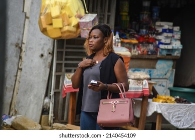 Abidjan, Ivory Coast- March 19, 2022: Young Woman Standing Outdoor Wiping Her Chest With Tissue While Holding Mobile Phone.