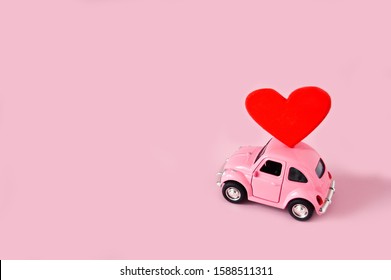Abinsk, 12 14 2019: Pink retro toy car lucky red heart on pink background. March 8, International Happy Women's Day, February 14 card, Valentine's day. Love concept.Cope space.