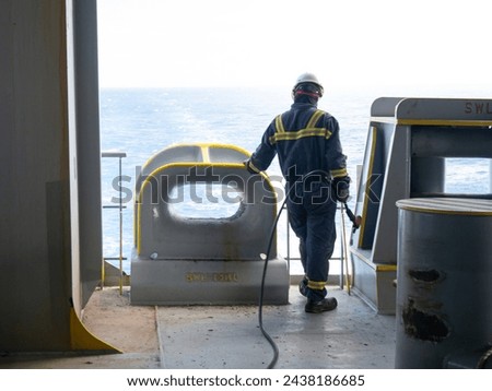 Able seaman crew member of cargo vessel is chipping rust from the ship bollard construction by air hammer and doing maintenance dressed in personal protective equipment