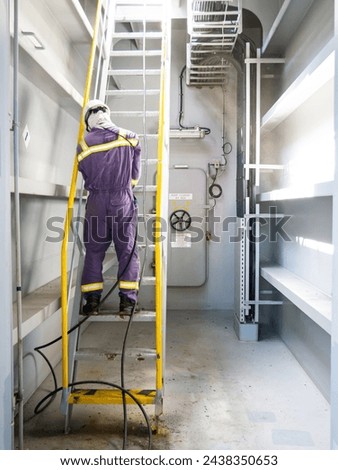 Able seaman crew member of cargo vessel is chipping rust from the ship ladder construction by air hammer and doing maintenance dressed in personal protective equipment