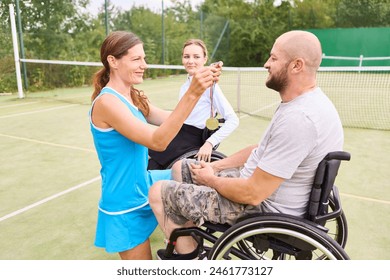 An able-bodied female tennis player awards a gold medal to a smiling male wheelchair athlete on a tennis court, celebrating his achievement. - Powered by Shutterstock