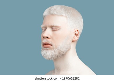 Abnormal deviations concept. Young extraordinary albino man with closed eyes, pale skin and white hair posing against turquoise background, free space. Skin abnormality and albinism concept