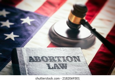 Abortion law in USA concept. Pregnancy termination ban. Judge gavel and Abortion Law book on US flag, close up view 
