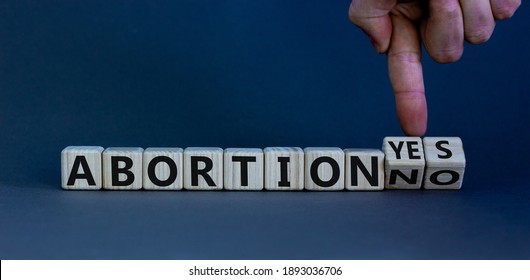 Abortion yes or no symbol. Male hand turns wooden cubes and changes words 'abortion yes' to 'abortion no' or vice versa. Beautiful grey background. Abortion yes or no concept, copy space.