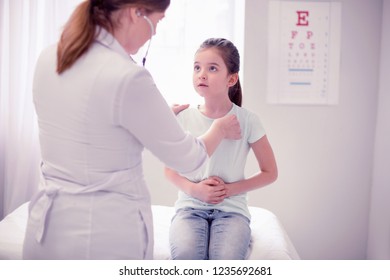 About Pain. Little Dark-haired Girl Wearing Jeans And Shirt Telling About Her Pain Professional Skillful Doctor