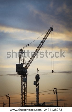 about a twin tower crane at the construction building working through sunset