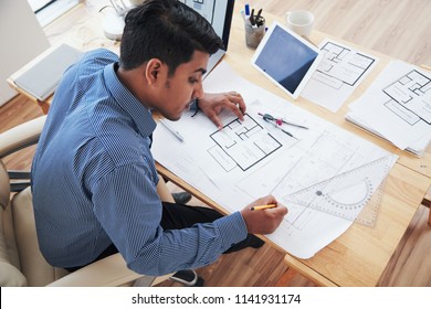 From Above Adult Indian Architect Working On Blueprint While Sitting At Desk In Office