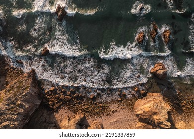 From above aerial view of foamy sea waves splashing near rocks on Ursa Beach on stormy day in Portugal