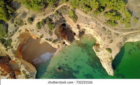 From above aerial view of rough cliffs on shoreline of tropical ocean with green water washing white sands in lagoon, Portugal, Algarve.