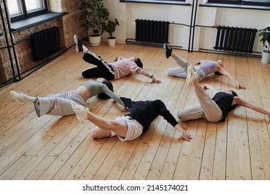Above angle of group of teenagers lying on wooden floor and learning new movements during vogue dance training in loft studio