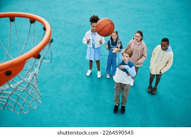 Above angle of intercultural schoolchildren playing basketball on playground together while one of them throwing ball into basket - Powered by Shutterstock