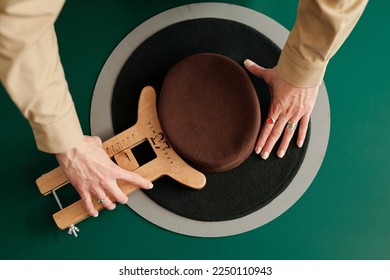 Above angle of pork pie hat and hands of young craftswoman with wooden tool for making necessary shape of new headcloth - Powered by Shutterstock