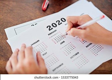 From Above Anonymous Freelancer Circling Date On Year 2020 Calendar While Working At Desk In Home Office