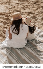 From Above Anonymous Mom And Kid In White Dresses And Straw Hats Sitting On Striped Blanket While Spending Sunny Summer Day On Sandy Beach