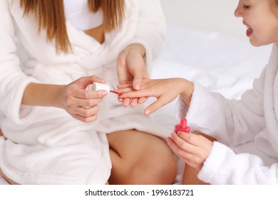 From Above Anonymous Woman In Bathrobe Painting Nails Of Girl While Sitting On Bed At Home