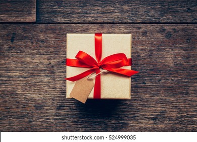 Above brown gift box and red ribbon with tag on wood background with space. - Powered by Shutterstock