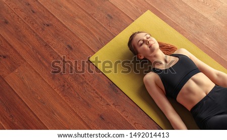 From above calm fit woman relaxing and breathing while lying at corpse pose on mat
