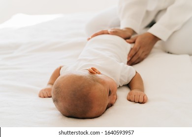 From Above Of Caring Mom With Newborn Mother Patting Infant Asian Little Child Lying On Tummy In Bedroom At Home