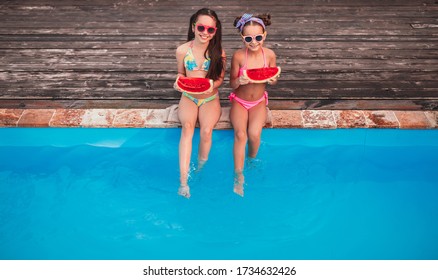 From above cheerful girls with pieces of ripe watermelon smiling and swinging legs in clean pool water while resting on resort together - Powered by Shutterstock