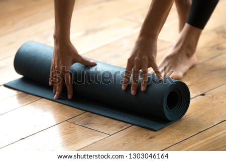 Above close up view of female hands rolling blue exercise mat on the floor after finishing her training session in yoga studio club or at home. Equipment for fitness, pilates, yoga, well being concept
