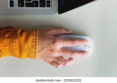 From above, close-up photo of a hand with a wireless white computer mouse to search for the necessary information, on the desktop