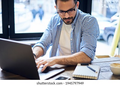 From Above Of Concentrated Bearded Male Remote Worker In Casual Outfit And Eyeglasses Typing On Laptop Keyboard During Work In Cafe