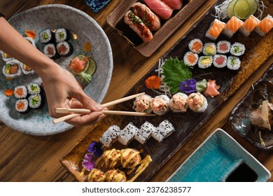 From above of crop anonymous person with chopsticks eating assorted sushi rolls served on tray at wooden table in cafe - Powered by Shutterstock